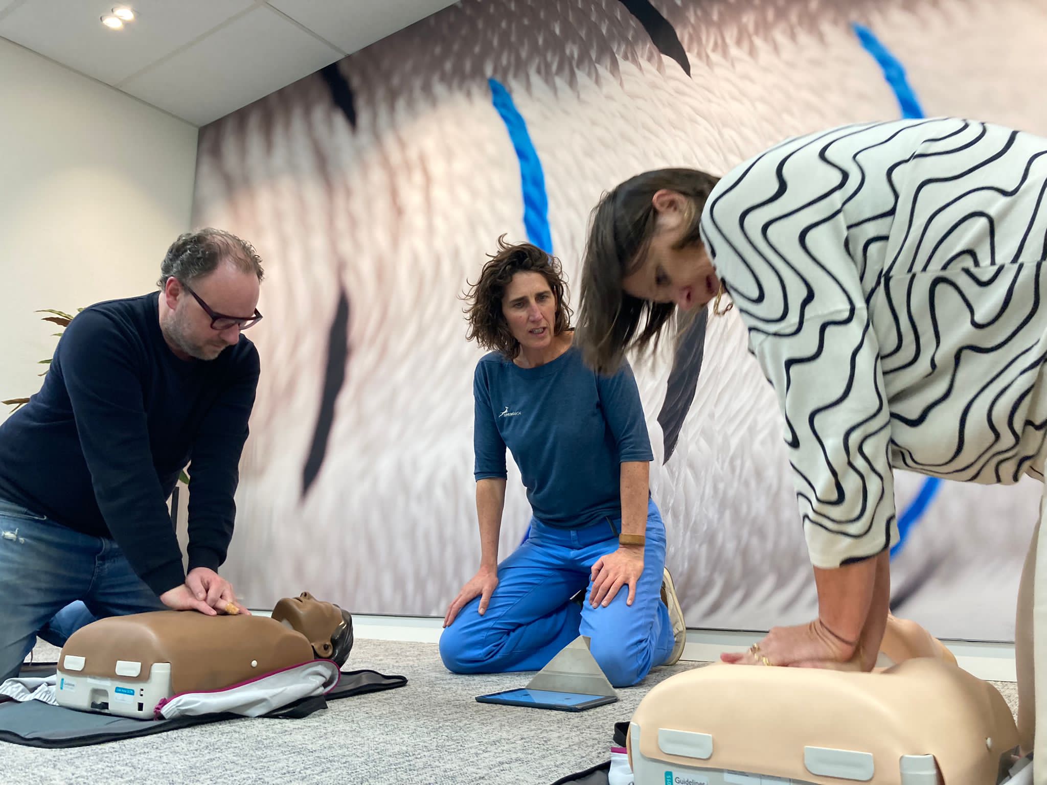 Coach helpt twee deelnemers met hun reanimatietechnieken